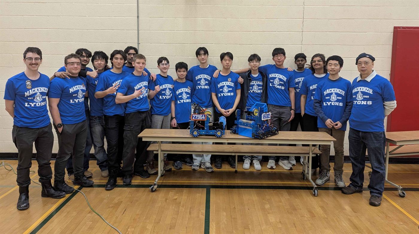 The WLMAC Robotics team in blue Mackenzie Lyons shirts, posing in the school gym with both competition robots